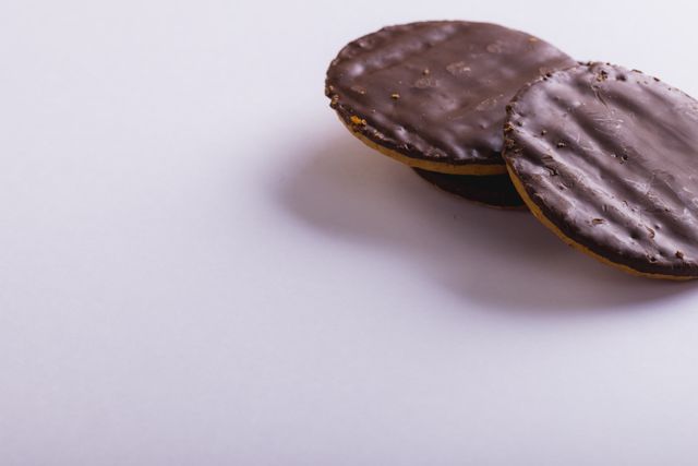 This image showcases a close-up of two chocolate-covered cookies against a plain white background, making them the focal point. Ideal for use in food blogs, recipe websites, digital menus, culinary advertisements, and promotional materials for bakeries and confectioneries. Perfect for articles about baking, desserts, and indulgent treats.