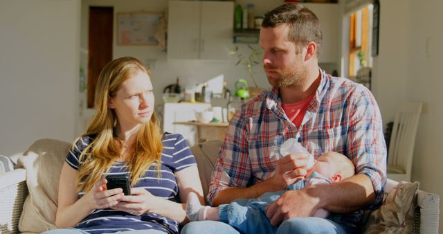 Concerned Parents Sitting on Couch with Baby Feeding Milk Bottle - Download Free Stock Images Pikwizard.com