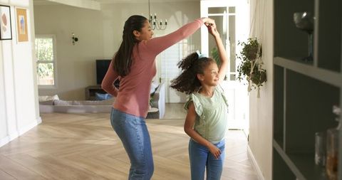 African american mother and daughter dancing and twirling in sunlit open-plan living room