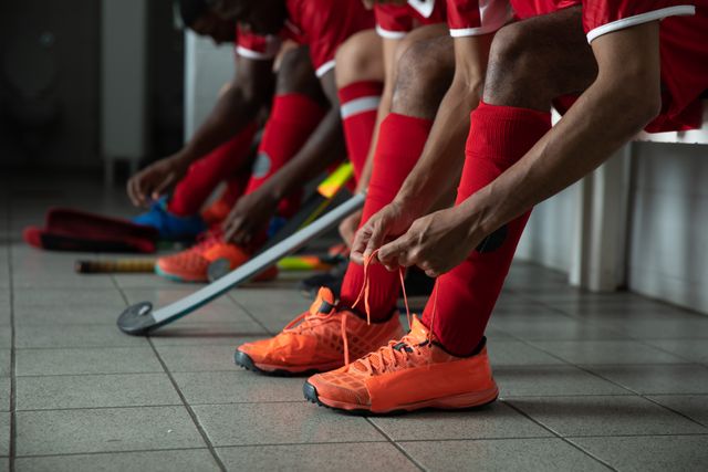 Side view of a multi-ethnic group of teenage male field hockey players, preparing before a game, sitting in the changing room, tying shoelaces and focusing. Sport game competition.
