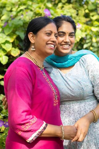 Smiling indian mother and daughter posing outdoors in traditional dress