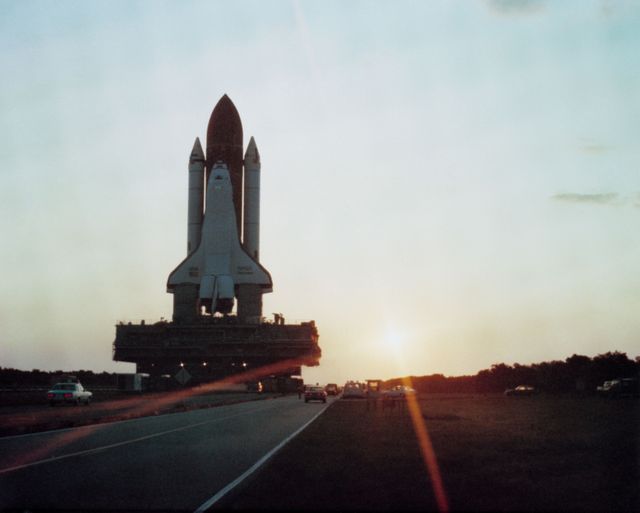 Space Shuttle Discovery is transported to the launch pad at sunrise in preparation for its maiden flight in 1984. This historic event includes a crew of six astronauts and is scheduled for a 41-D mission deploying Syncom IV-1 (LEASAT) and includes diverse payloads such as the OAST-1, Large Format Camera, IMAX, and Cinema 360 cameras. Ideal for use in content related to space exploration history, NASA achievements, astronaut missions, and 20th-century technological advancements.