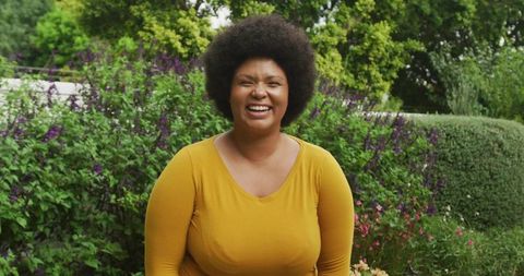 Joyful woman laughing in vibrant garden wearing mustard yellow top, wellness lifestyle