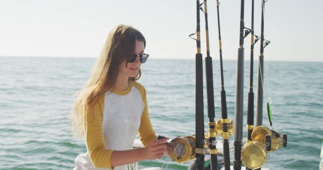 Happy caucasian teenage girl inspecting fishing rod on deck of a boat in the ocean on a sunny day. Leisure, hobbies, free time, travel and vacations.