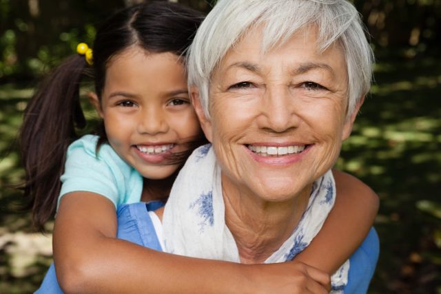 Close-up portrait of smiling grandmother giving piggyback to granddaughter at backyard