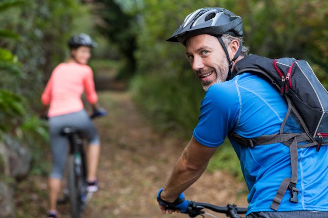 Couple enjoying a cycling adventure through a forest trail, promoting outdoor activities and a healthy lifestyle. Ideal for use in advertisements for fitness gear, outdoor recreation, travel brochures, and health and wellness campaigns.