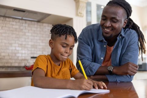 African american dad helping son with homework at kitchen table, warm supportive parenting