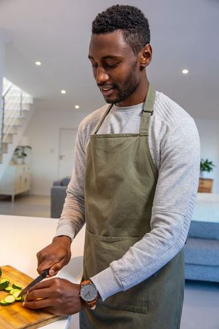 Mid Adult Man Wearing Apron Slicing Zucchini in Modern Kitchen