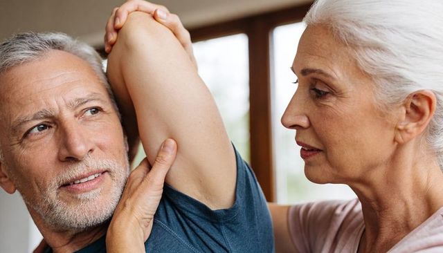 Senior couple doing assisted shoulder stretch at home, gentle mobility care and companionship