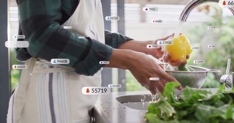 Woman washing bell pepper with digital notifications in kitchen