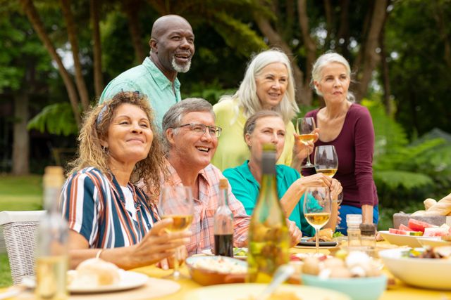 Multiracial senior male and female friends having wine at table during backyard party. unaltered, lifestyle, leisure, togetherness, friendship and backyard party.