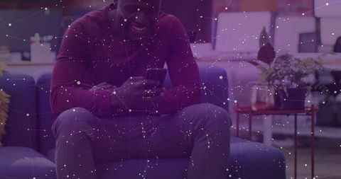 African American man checking smartphone on coworking sofa with purple network overlay