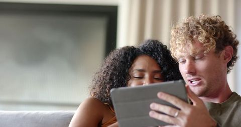 Couple relaxing on light sofa viewing gray folio tablet together in cozy daylight room