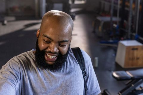 Smiling african american man leaving gym carrying backpack and wearing gray t-shirt