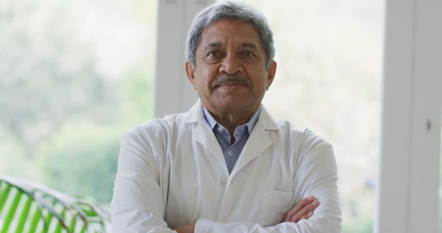 Senior doctor wearing white lab coat crossing arms and staring forward confidently. Ideal for healthcare-related content, advertisements for medical services, doctor consultations, and professional health articles.