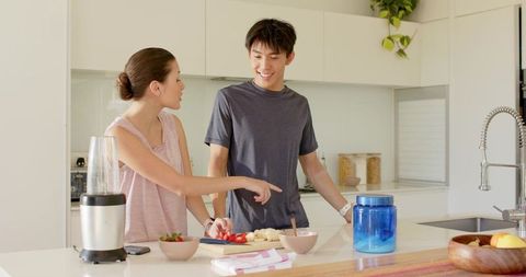 Couple preparing smoothie and chopping strawberries on bright modern kitchen island