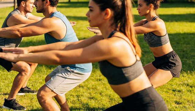 Performing group outdoor squat workout in park, fitness class and team training
