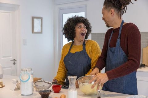 African american couple baking together in bright kitchen, mixing batter and smiling