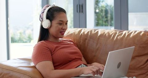 Asian Woman Relaxing at Home Working on a Laptop with Headphones