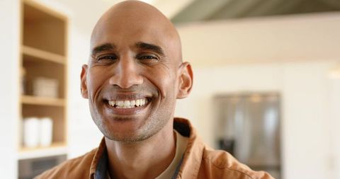 Smiling bald man portrait in warm modern kitchen conveying friendly confident expression