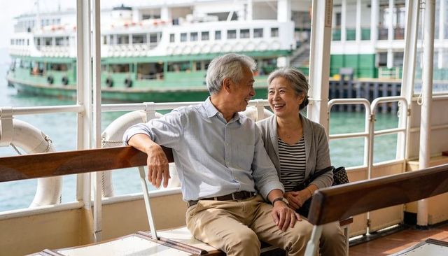 Senior asian couple laughing and talking on ferry bench overlooking busy harbor