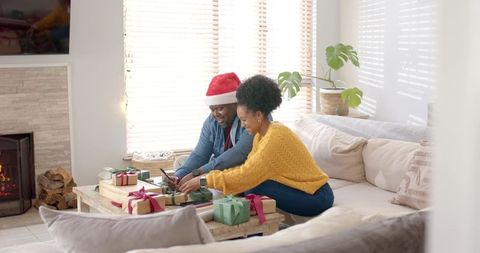 Diverse couple unwrapping christmas gifts on cozy living room sofa by fireplace
