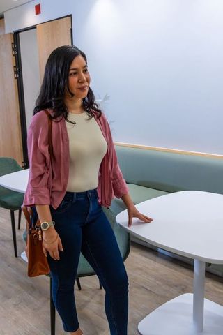 Young woman standing in modern office lounge resting hand on table holding leather shoulder bag