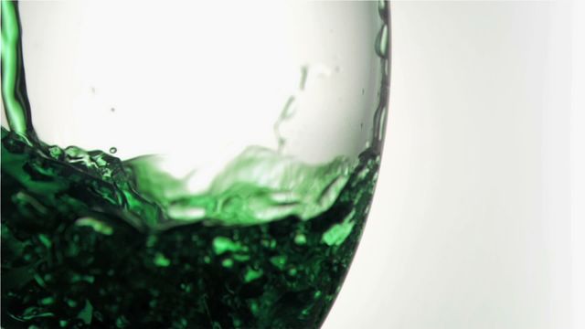 The vivid green liquid flows elegantly into the transparent glass, creating intriguing patterns as light filters through. Perfect for use in advertising, illustrating freshness, vitality, or in scenes involving creative product presentation. An ideal fit for promotional visuals related to beverages.