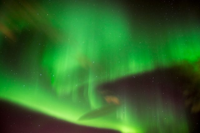 This image showcases the stunning northern lights radiating green hues across a dark night sky, with twinkling stars in the background. Ideal for use in nature and astronomy-related articles, travel brochures focusing on Arctic and polar regions, and educational material on natural phenomena. Suitable as a background for digital content highlighting aurora imagery.
