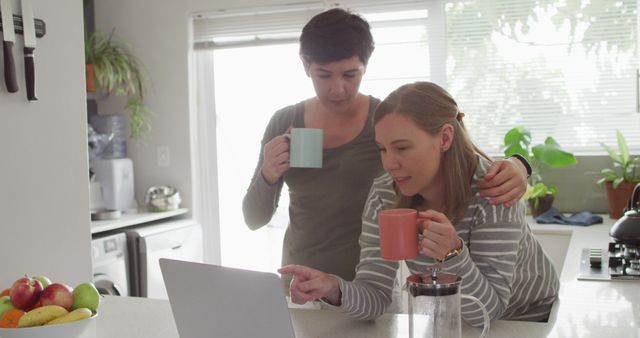 Caucasian lesbian couple holding coffee cups using laptop at home. lgbt relationship and lifestyle concept