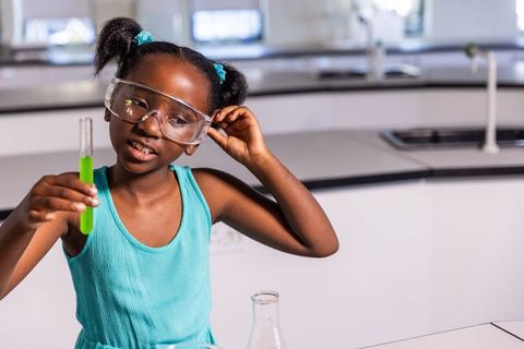 African american girl holding green test tube wearing safety goggles in science lab