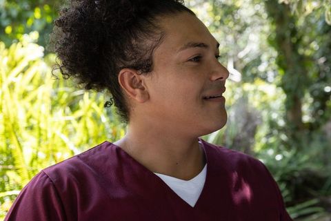 Healthcare worker wearing maroon scrubs speaking outdoors in lush garden portrait medical