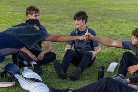 Teen cricket team relaxing on grass fist-bumping after practice