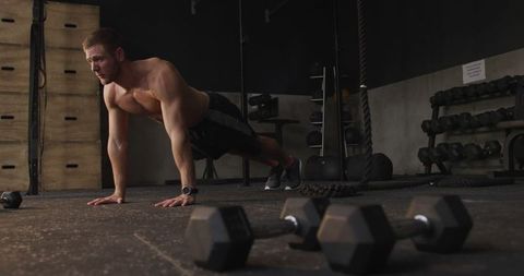 Fit Man Performing Push-Ups in Gym with Dumbbells in Foreground