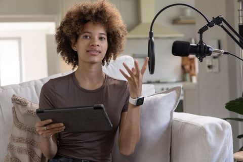 African american woman recording home podcast on tablet with professional microphone
