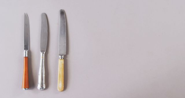 Three different knives with varying handle designs are laid out on a plain background, with copy space. Their arrangement suggests a focus on cutlery design or a culinary theme.