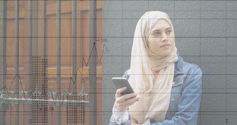 Young muslim woman in beige hijab holding smartphone with financial analytics overlay
