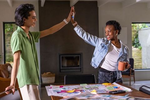 High-fiving diverse colleagues collaborating on creative project planning with sticky notes