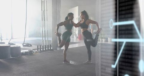 Two women stretching in gym holding foot balance against wall, strength training overlay