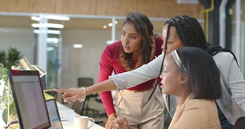 Multiracial women collaborating around laptop in modern office brainstorming session