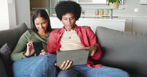 Modern couple relaxing on sofa with tablet and smartphone