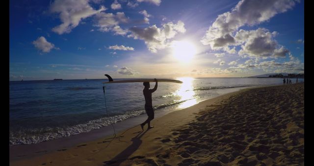Young Pacific Islander man carries a surfboard on the beach at sunset. He enjoys a serene evening by the sea, ready for a surfing session.
