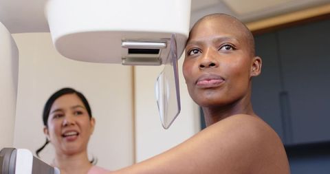 Black woman undergoing mammogram with technologist operating digital mammography paddle