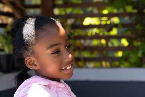 Preteen african american girl smiling and looking right, sunlit backyard trellis greenery