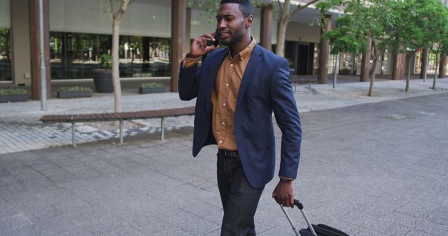 Businessman walking outside a modern office building, pulling a suitcase and talking on the phone. Ideal for use in articles related to business travel, corporate lifestyle, professional communication, and modern office environments.