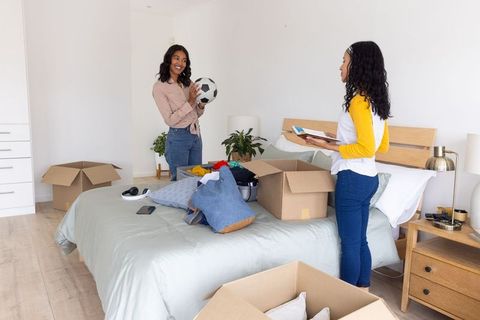 Friends unpacking moving boxes in new home's bedroom