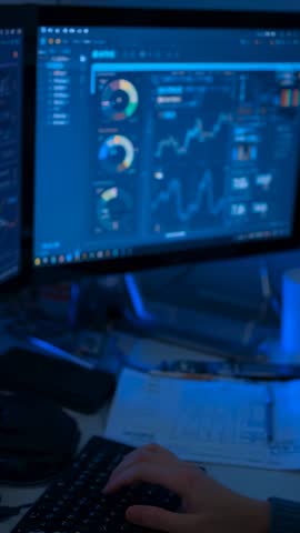 Typing and Navigating Interactive Data Dashboard on Dual Monitors in Dimly Lit Office