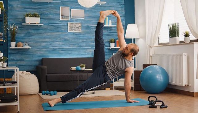 Man performing one-arm side plank with leg hold in modern living room home workout