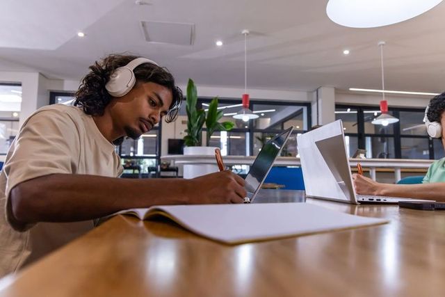 Young diverse men studying with laptops and headphones in bright coworking space