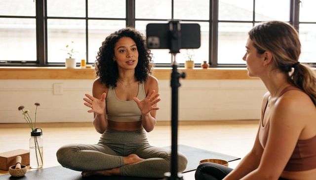 Yoga instructor teaching on-camera guided class in sunlit studio with student